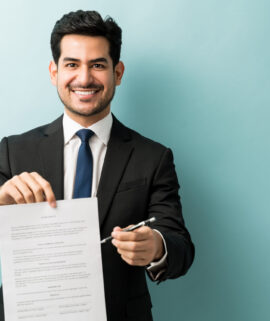 Portrait of smiling confident young male professional with contract against colored background